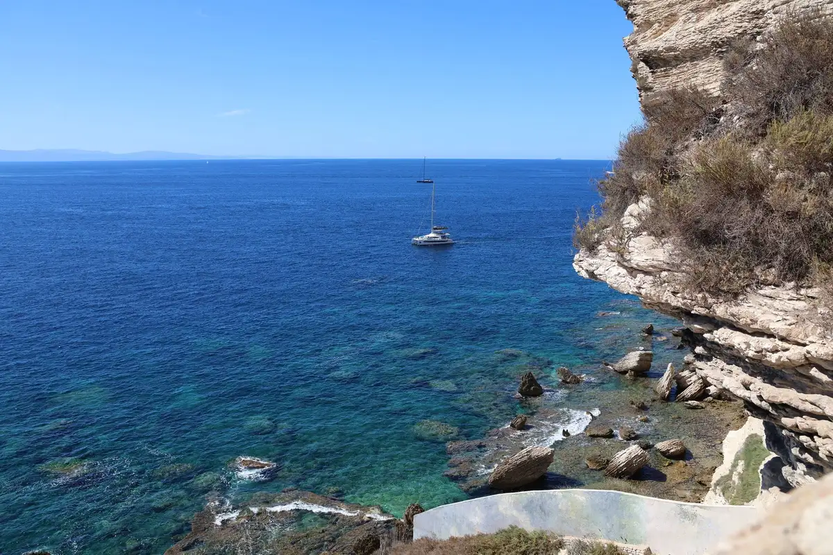 Vue aérienne d'une côte méditerranéenne avec falaises et un voilier en navigation