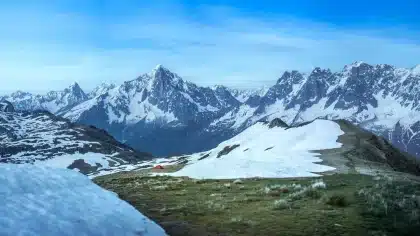 Randonneur en montagne sur un sentier alpin avec glaciers et sommets enneigés en arrière-plan
