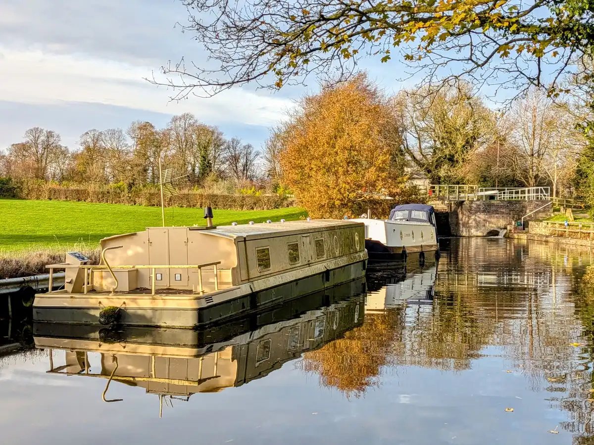 Péniche naviguant paisiblement sur un canal bordé d'arbres, avec une tour médiévale en arrière-plan