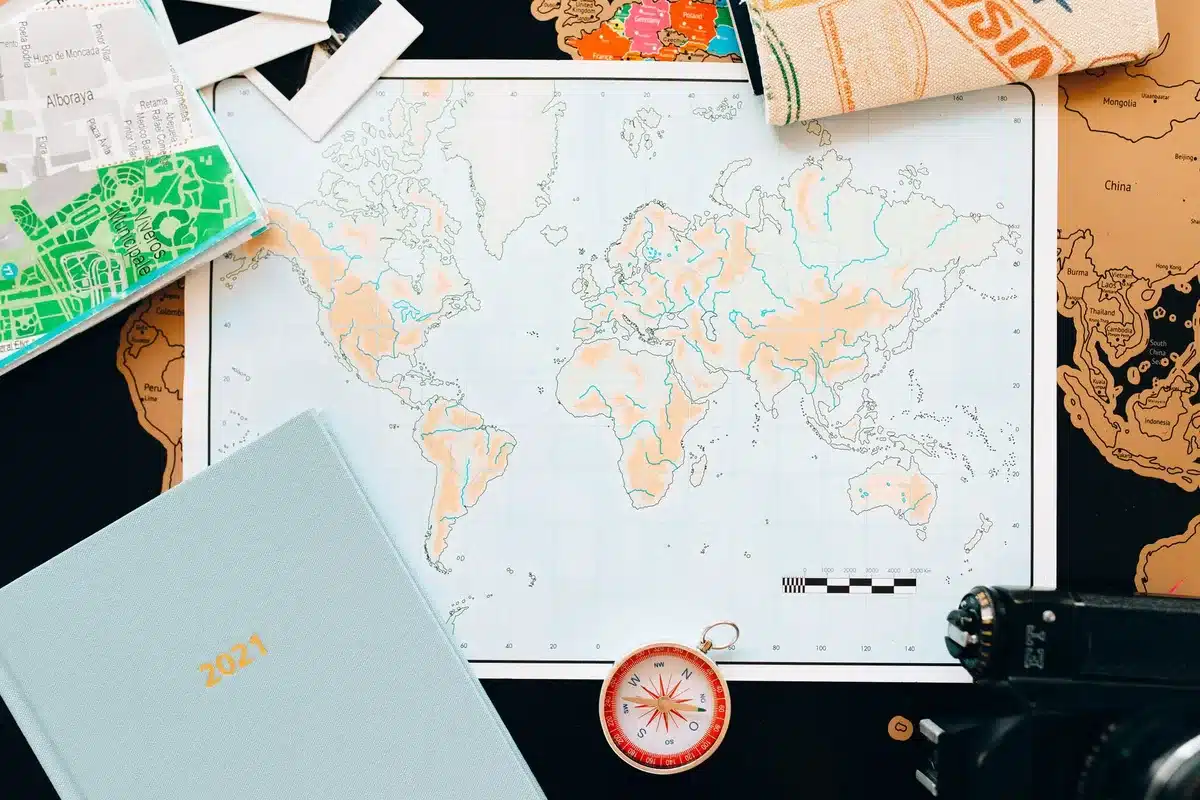 Voyageur consultant une carte devant un paysage montagneux ou côtier, avec ses bagages à proximité
