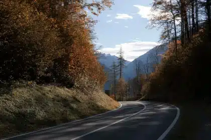 Un camping-car circulant sur une route de montagne sinueuse avec des sommets alpins et un lac en arrière-plan