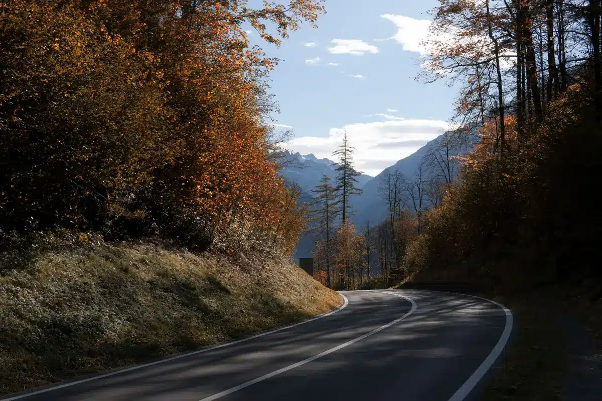 Un camping-car circulant sur une route de montagne sinueuse avec des sommets alpins et un lac en arrière-plan