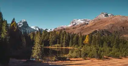 Randonneur contemplant un lac alpin en forme de cœur au coucher du soleil automnal, entouré de montagnes dorées