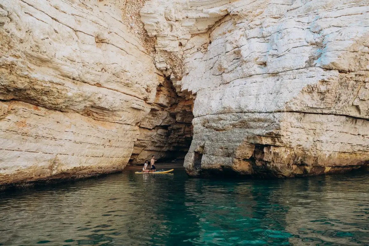 Personne en kayak explorant l'entrée d'une grotte côtière depuis la mer
