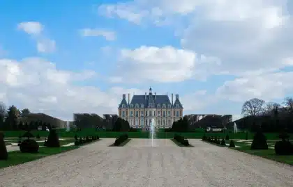 Château majestueux avec jardins à la française, allées ornementales et visiteurs en arrière-plan