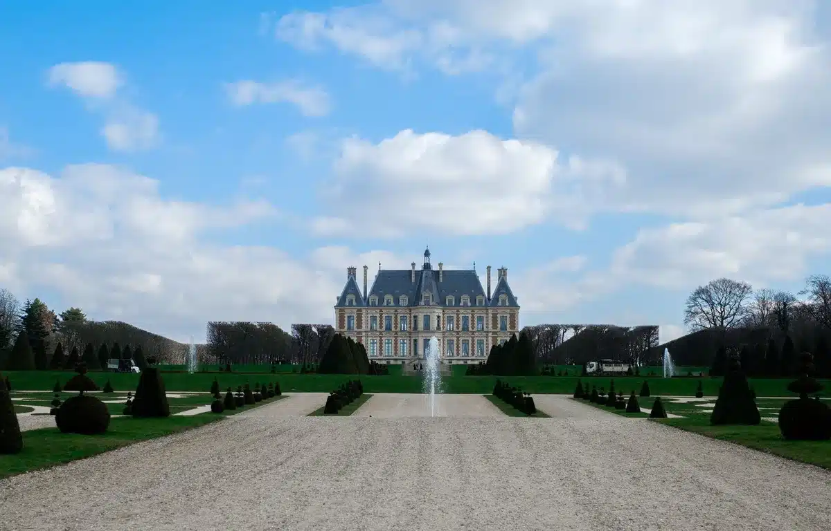 Château majestueux avec jardins à la française, allées ornementales et visiteurs en arrière-plan