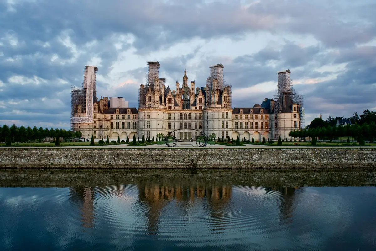 Château de la Loire aux façades ornées se reflétant dans l'eau calme, entouré de jardins et de forêts