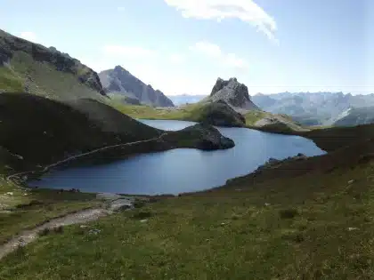 Randonneur sur un sentier alpin avec lacs turquoise et crêtes rocheuses en arrière-plan