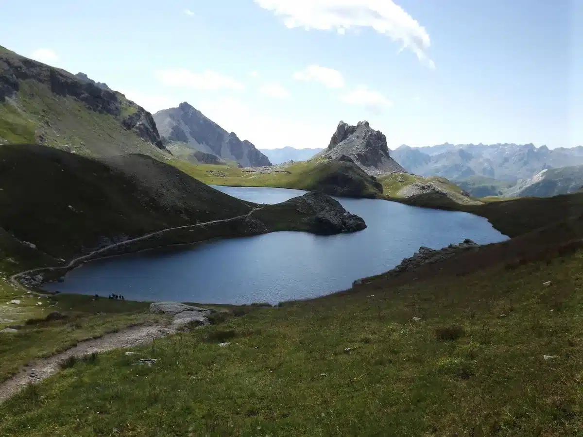 Randonneur sur un sentier alpin avec lacs turquoise et crêtes rocheuses en arrière-plan