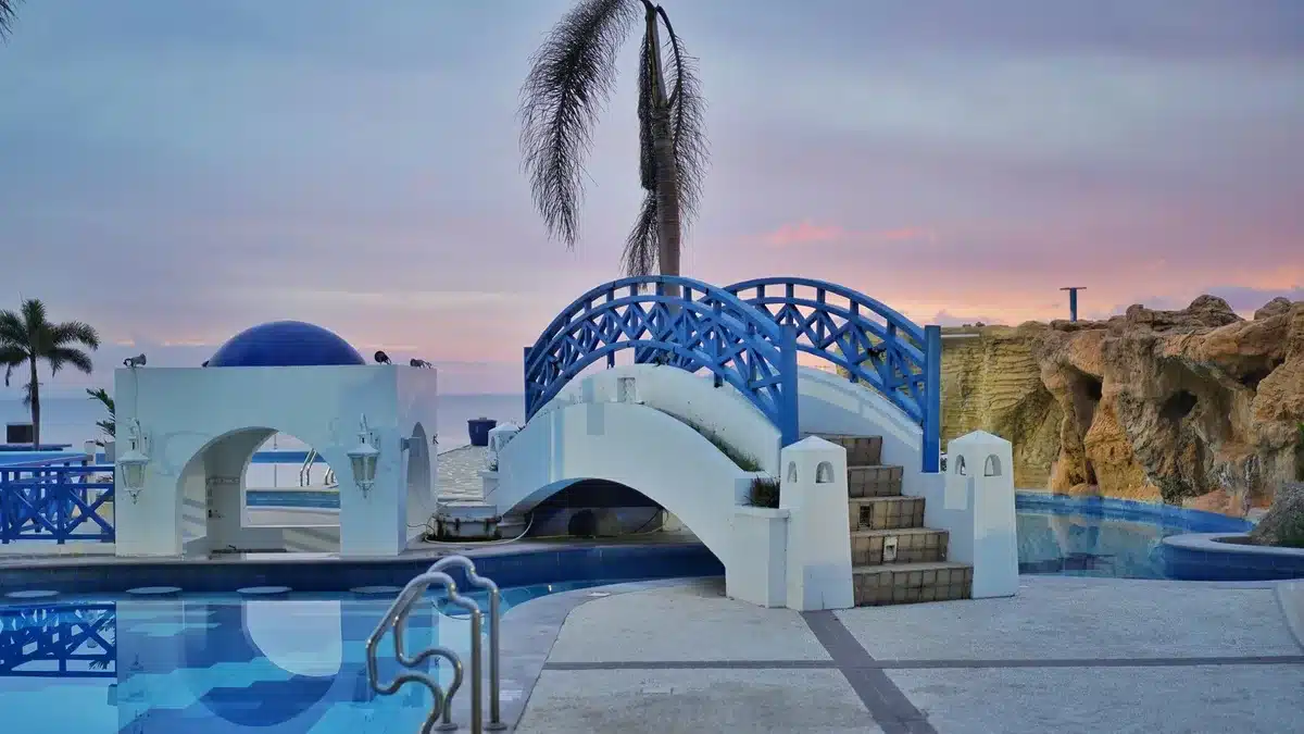 Piscine à débordement d'un resort de luxe face à la mer, au coucher du soleil, avec transats et palmiers