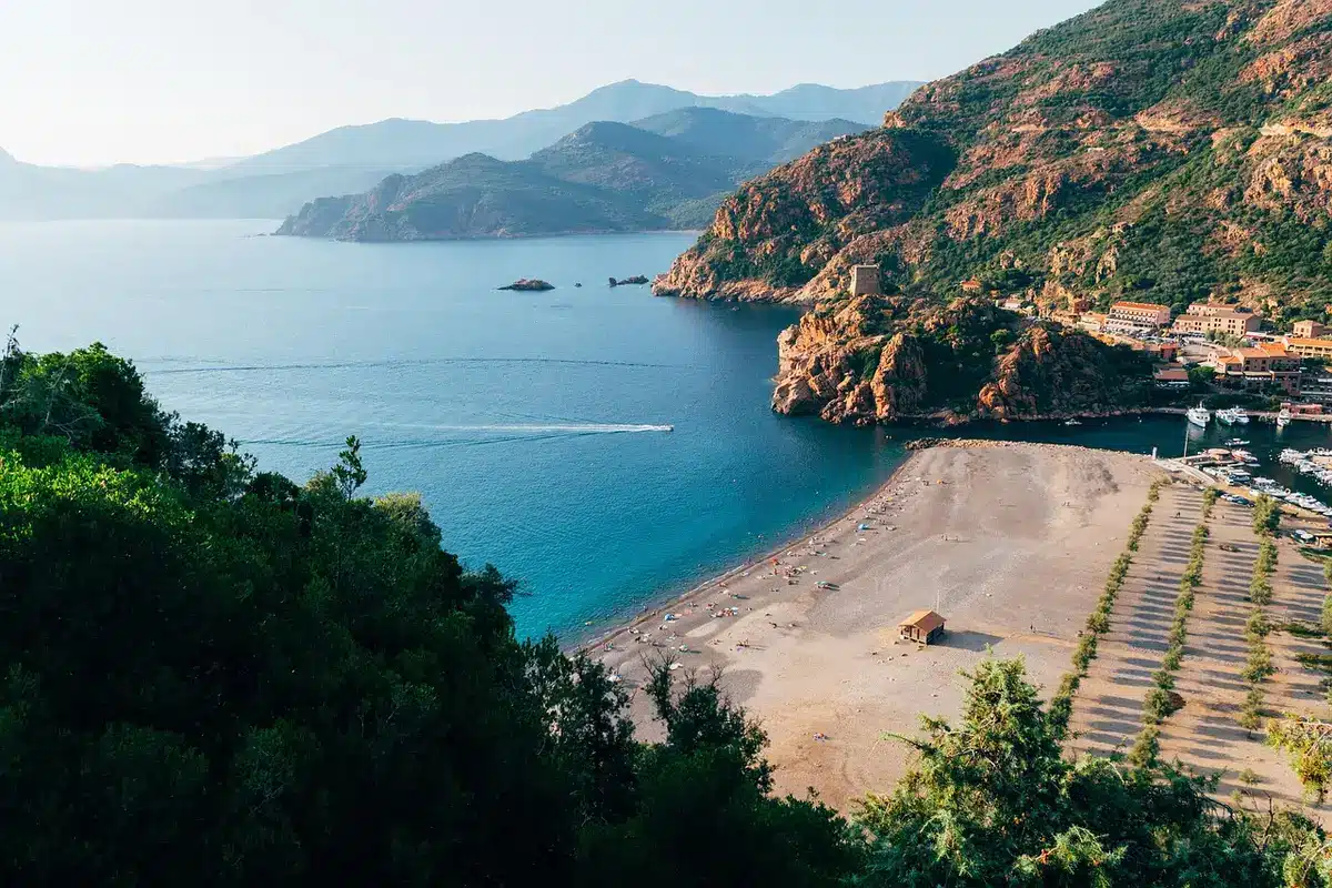 Plage méditerranéenne avec eau turquoise et montagnes en arrière-plan au lever du soleil