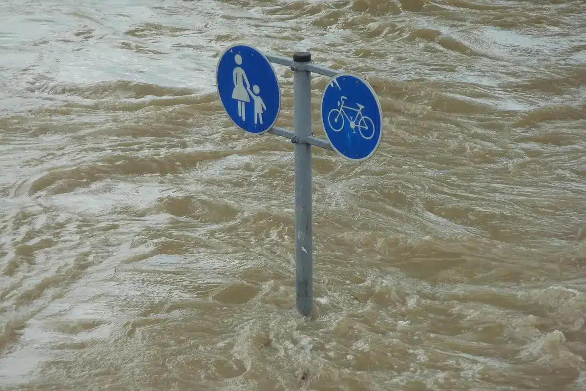 Vallée montagneuse endommagée par les crues, avec des eaux boueuses et une équipe de secours en arrière-plan