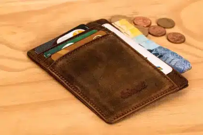 Main anonyme tenant des cartes bancaires sur une table avec carnet de budget et smartphone