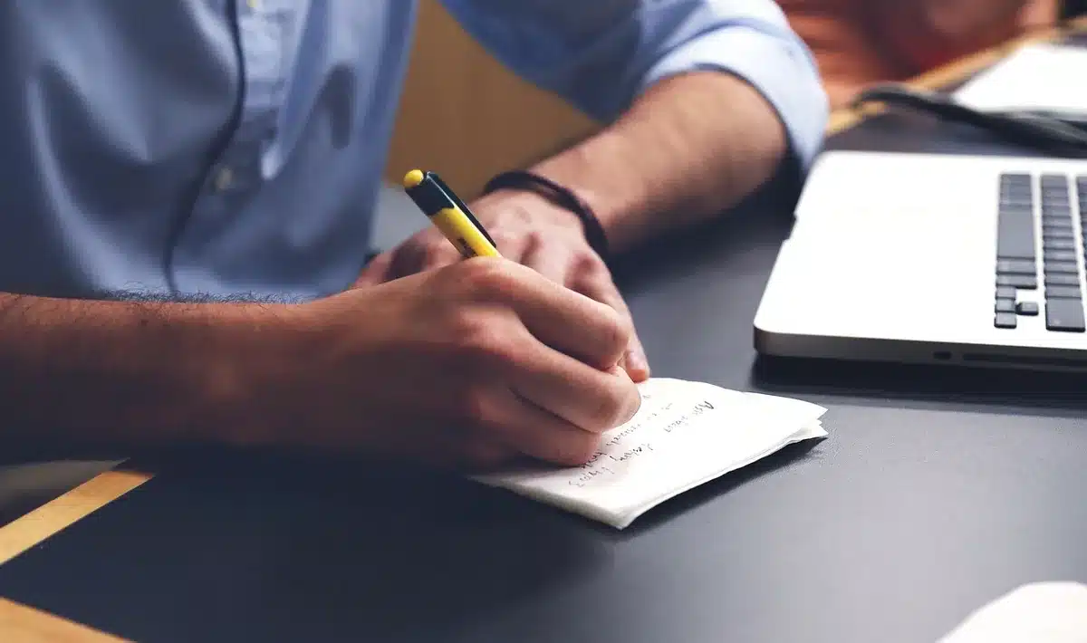 Main annotant une carte sur un bureau avec un ordinateur portable