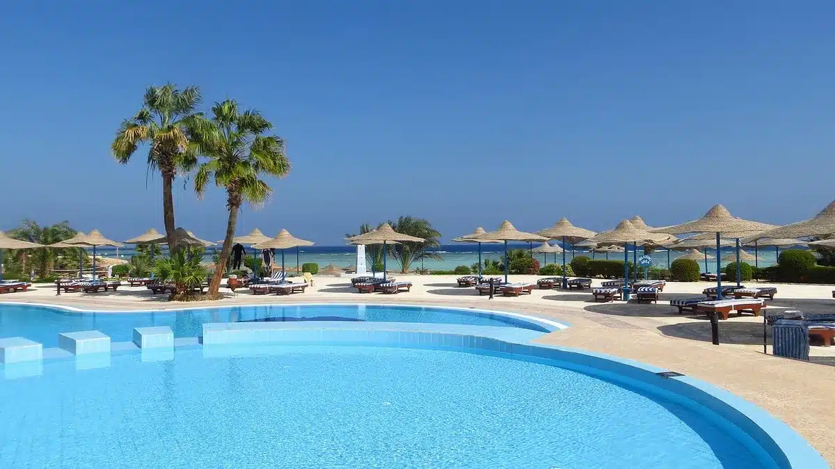Terrasse d'hôtel en journée avec piscine et chemin vers la plage, vue dallée