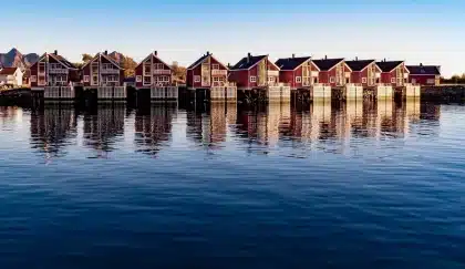 Rorbuer colorés le long d’un quai avec fjord et montagnes en arrière-plan, en plein jour