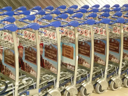 Hall d'aéroport en journée avec valises sur un chariot et mains tenant un billet